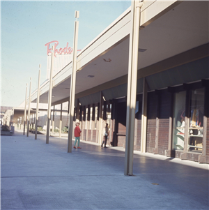 Two children stand outside a shopping center under a red sign that says Rhodes. 